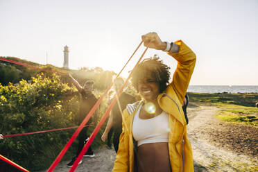 Determined woman pulling resistance band during group training at beach - MASF41560