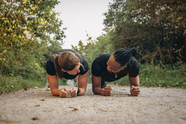 Young man practicing plank position with woman on footpath - MASF41562