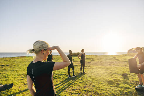 Woman shielding eyes during group training on sunny day at beach - MASF41564