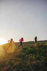 Women running up on hill during group training session against sky - MASF41578