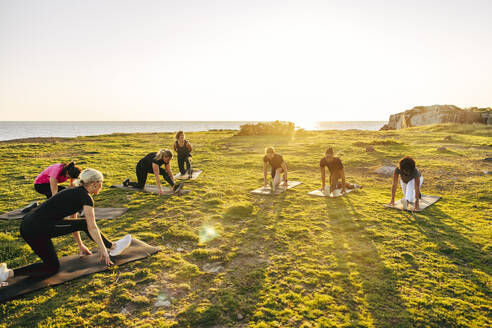 Team doing stretching on grass during group training session near sea against sky - MASF41579