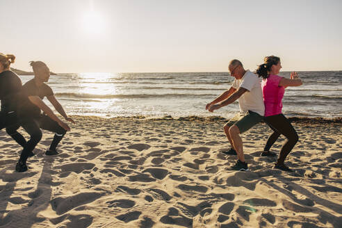 Team exercising with each other on sand during group training session at beach - MASF41589