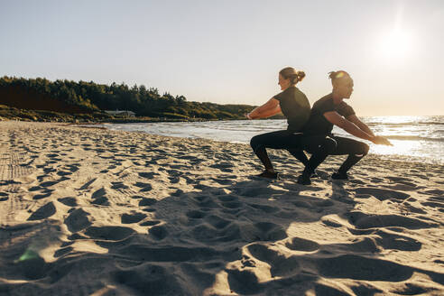 Man and woman practicing squats on sand at beach - MASF41590