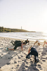 Male and female teammates exercising on sand during group training session at beach - MASF41591