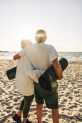 Elderly senior couple standing with arms around while standing at beach - MASF41601
