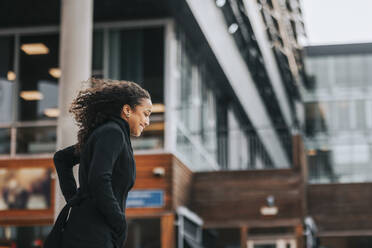 Side view of smiling businesswoman walking in front of building - MASF41615