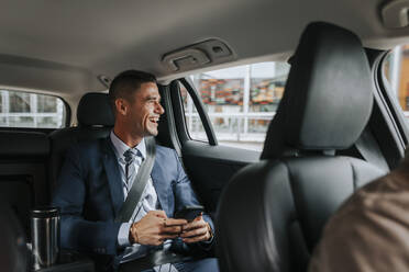 Happy businessman looking through window while sitting in taxi - MASF41634