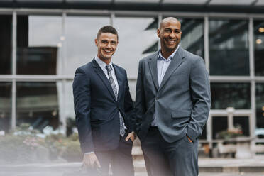 Portrait of smiling male corporate professionals wearing suit while standing in front of building - MASF41635