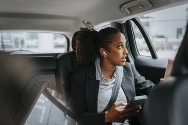 Businesswoman looking through window and talking on smart phone while sitting in car - MASF41652