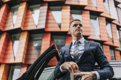 Low angle view of businessman standing near car in front of building - MASF41655