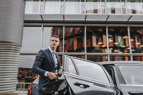 Businessman disembarking from car in front of building - MASF41656