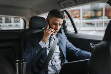 Businessman talking on smart phone while sitting with laptop in car - MASF41657