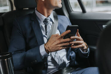 Midsection of businessman holding smart phone while sitting in car - MASF41659