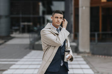 Businessman wearing wireless in-ear headphones while standing at street - MASF41660