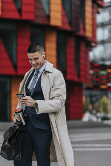 Happy businessman using smart phone while standing at street - MASF41661
