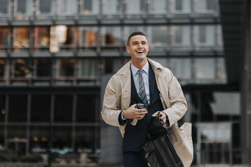 Happy businessman laughing while walking in front of office building - MASF41664