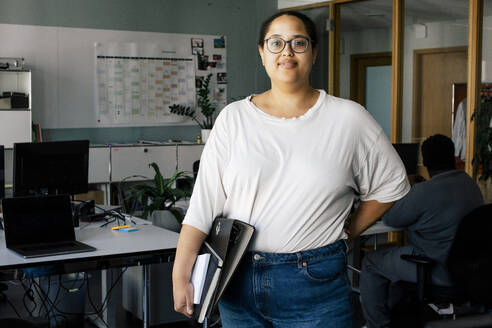Portrait of smiling female business professional standing with hand on hip at coworking office - MASF41667