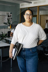 Portrait of female computer programmer holding files while standing at office - MASF41668