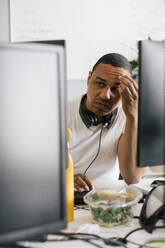 Worried male entrepreneur with head in hand sitting at desk in office - MASF41677