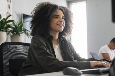 Smiling businesswoman with curly hair working at office - MASF41685