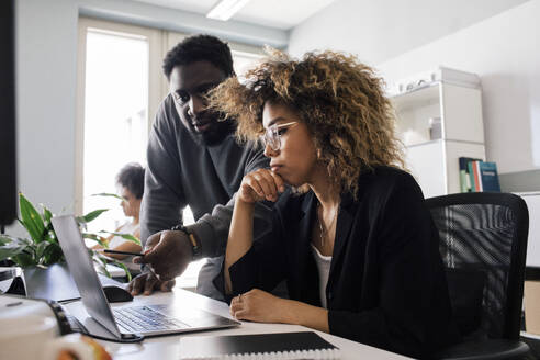 Male colleague discussing over laptop with female entrepreneur sitting at office - MASF41700