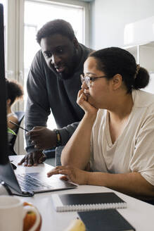 Male colleague discussing with female coworker sitting with hand on chin at office - MASF41701