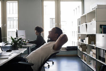 Side view of smiling businessman resting while sitting on chair at office - MASF41708