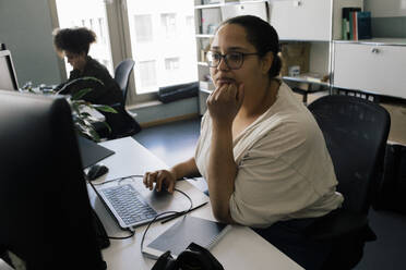 Businesswoman with hand on chin using computer while sitting at desk in office - MASF41710