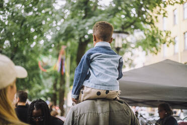 Rear view of man carrying son on shoulder at flea market - MASF41722