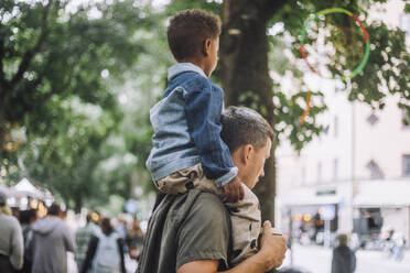 Side view of boy sitting on father's shoulder while shopping at flea market - MASF41728