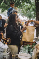 Smiling woman holding paper bag while doing shopping with family at flea market - MASF41729