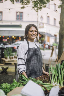 Portrait of smiling female vendor selling vegetables at organic market - MASF41738