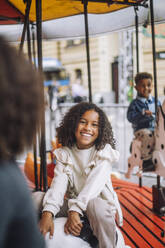 Portrait of smiling girl with curly hair enjoying during ride on carousel at amusement park - MASF41754