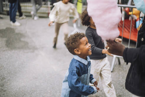 Excited boy looking at mother holding cotton candies at amusement park - MASF41757