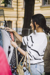 Side view of woman choosing dress from rack while shopping at flea market - MASF41768