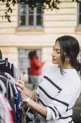 Young woman buying dress while doing shopping at flea market - MASF41769