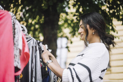 Low angle side view of smiling woman buying dress at flea market - MASF41770