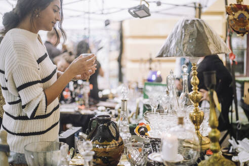 Side view of young female customer buying antique during shopping at flea market - MASF41772