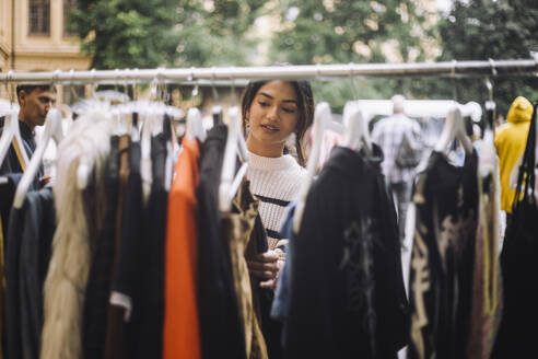 Young woman selecting dress hanging on clothes rack at flea market - MASF41774