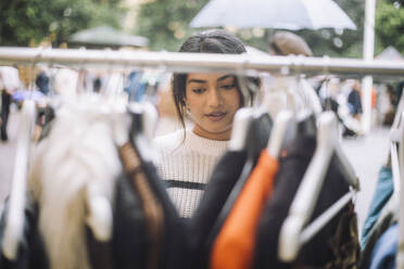 Young female customer buying dress hanging on rack at flea market - MASF41775