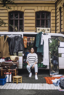 Portrait of smiling woman selling second hand goods while sitting in van at flea market - MASF41777