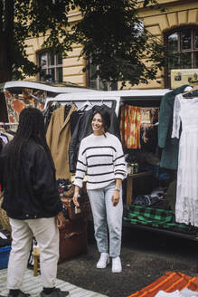 Smiling female owner welcoming customer during during second hand sale at flea market - MASF41780