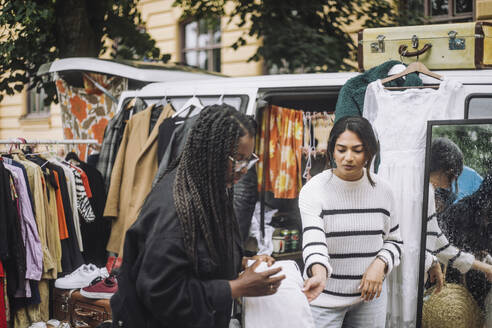 Female owner assisting customer shopping during during second hand sale at flea market - MASF41781