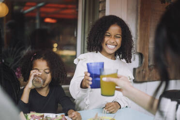 Cheerful girl toasting drinks with woman while having dinner at restaurant - MASF41792