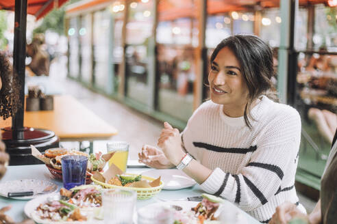 Smiling young woman having street tacos and snacks while sitting at restaurant - MASF41793