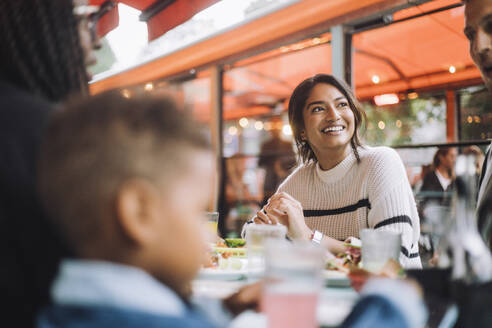 Smiling woman looking away while having food with family at restaurant - MASF41794