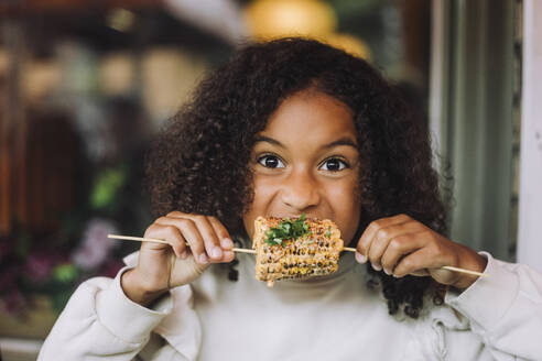 Portrait of hungry with curly hair eating corn at restaurant - MASF41796