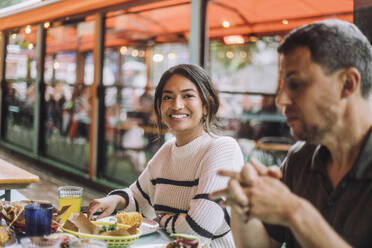 Portrait of smiling woman sitting with man while having food at restaurant - MASF41802