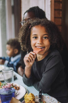 Portrait of smiling girl eating nacho chip sitting at restaurant - MASF41803