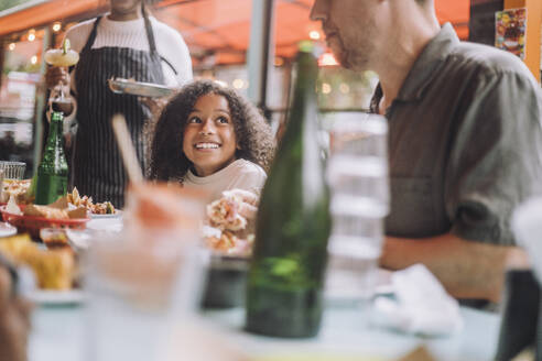 Smiling girl having food with father while sitting at restaurant - MASF41811